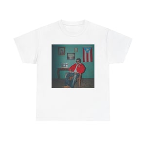 May include: White t-shirt featuring a printed image of a person in a red jacket and sunglasses, seated in a room with a Puerto Rican flag on the wall. The image has a vintage aesthetic.