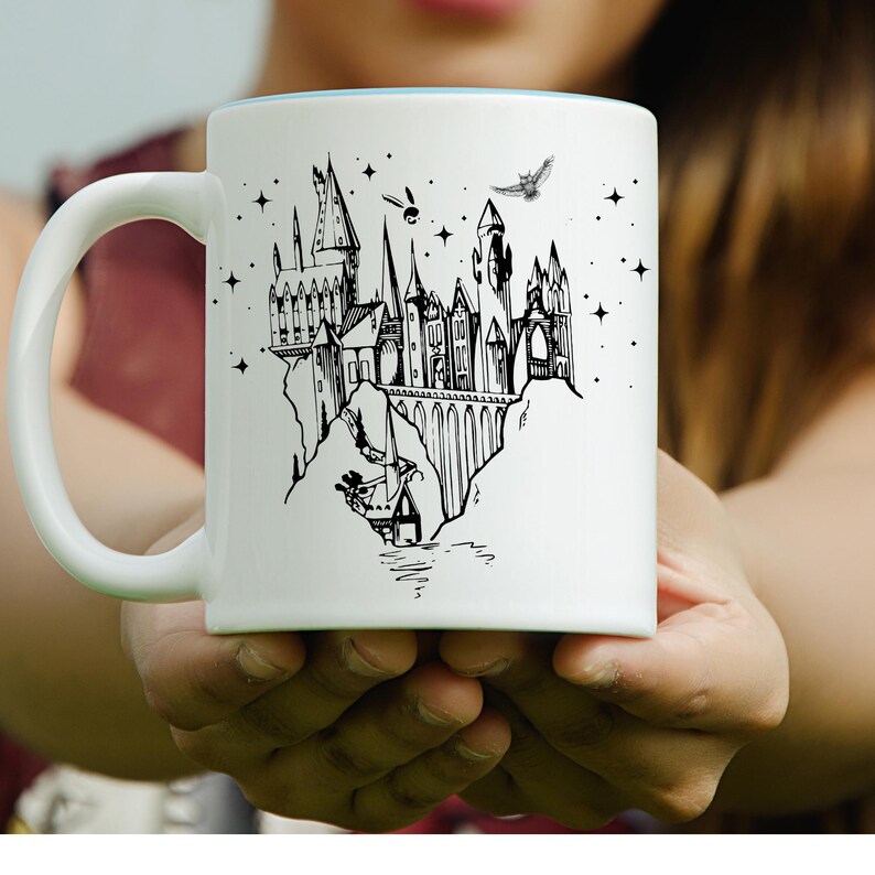 Może przedstawiać: Biały ceramiczny kubek z czarną ilustracją zamku, wież, łuk&oacute;w i gwiazd. Kubek ma jasnoniebieskie wnętrze i zakrzywiony uchwyt. W projekcie uwzględniono r&oacute;wnież latającego ptaka i inne drobne szczeg&oacute;ły.