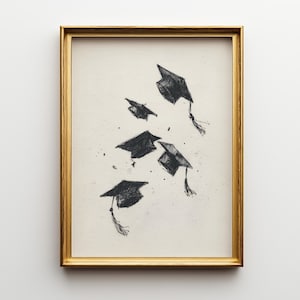 May include: A framed print featuring a pen and ink illustration of several graduation caps in mid-air. The caps are black with tassels, set against a cream-colored background. The frame is gold.
