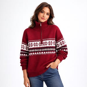 May include: A burgundy sweater with a high collar and a quarter-zip closure. The sweater features a white and black snowflake pattern across the chest and sleeves. The model is wearing blue jeans.