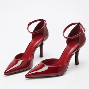 May include: A pair of glossy red high heels with pointed toes and ankle straps. The heels have a stiletto design and a small buckle closure. The shoes are a vibrant shade of red.