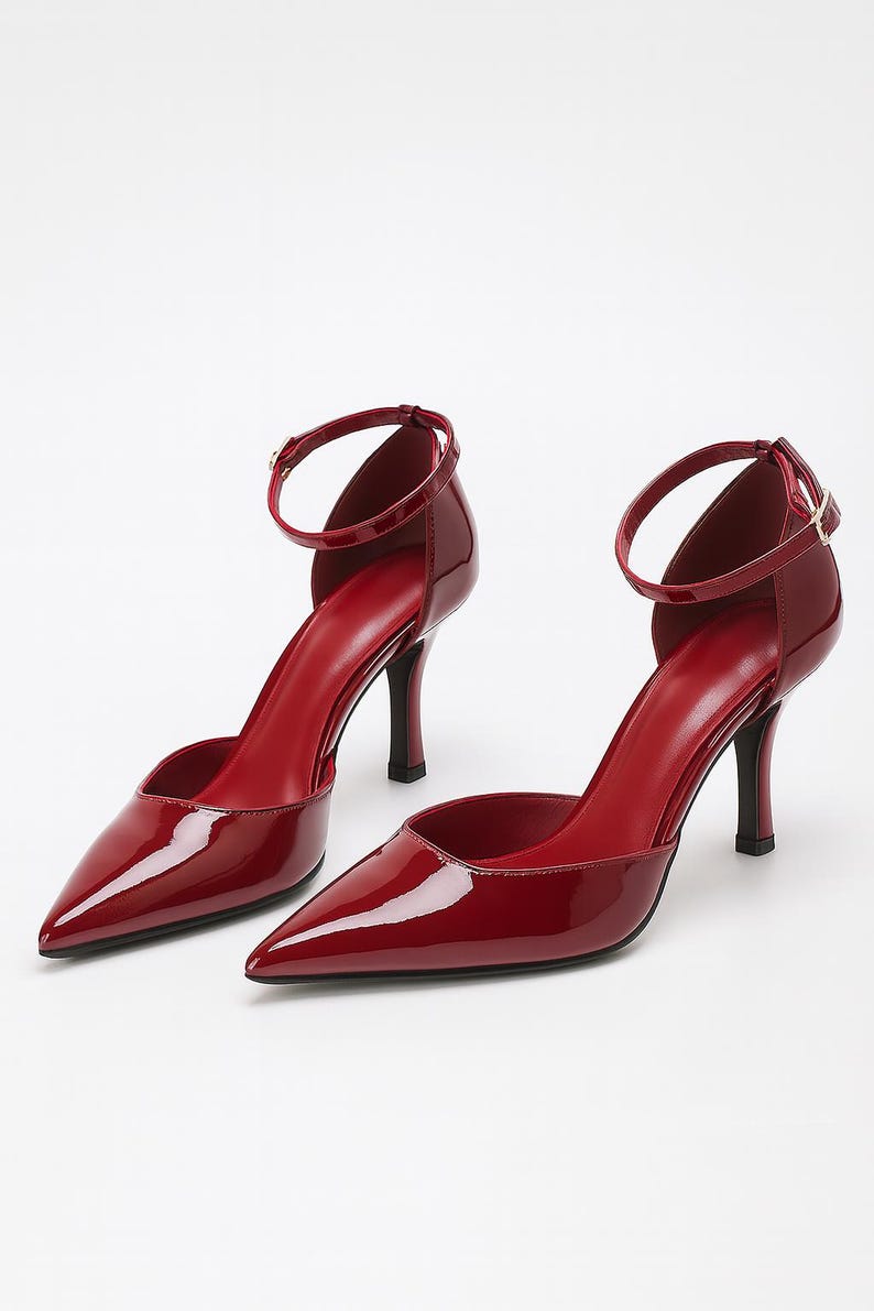 May include: A pair of glossy red high heels with pointed toes and ankle straps. The heels have a stiletto design and a small buckle closure. The shoes are a vibrant shade of red.