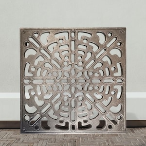 Può includere: Griglia quadrata in metallo color bronzo con un intricato design traforato. Il motivo presenta un motivo circolare centrale circondato da una serie di forme curve e lineari. La griglia è probabilmente per il drenaggio o la ventilazione.