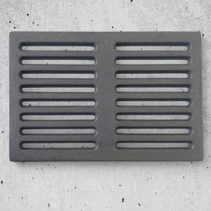 Puede incluir: Una cubierta de ventilación rectangular de metal gris oscuro con ranuras horizontales. La cubierta de ventilación es de hierro fundido y está diseñada para su uso en una chimenea u otro sistema de calefacción. La superficie tiene un aspecto ligeramente texturizado.