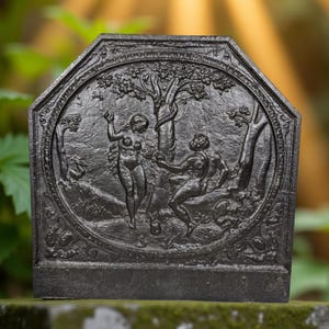 Op de afbeelding: Donkergrijze, achthoekige gietijzeren haardplaat met een reliëfsculptuur van twee figuren onder een boom. De figuren bevinden zich in een tuinsetting, met gedetailleerd gebladerte en een decoratieve rand. Het ontwerp is klassiek.