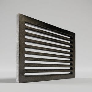 Peut inclure: Une grille de ventilation rectangulaire en métal gris foncé dotée d'une série de fentes horizontales parallèles. L'objet présente une finition mate texturée et un cadre épais, vu sous un angle latéral pour souligner la profondeur des ouvertures.
