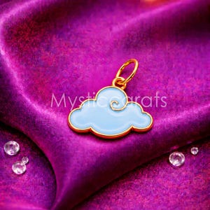 May include: A gold-coloured cloud charm with a light blue enamel fill and a gold-coloured swirl design. The charm is on a purple satin surface with the text "Mystic Carats".