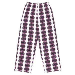 May include: White wide-leg pants with a vertical pattern of purple and black floral-like designs. The pants have a comfortable, relaxed fit, suitable for casual wear. The pattern repeats down the length of the pants.
