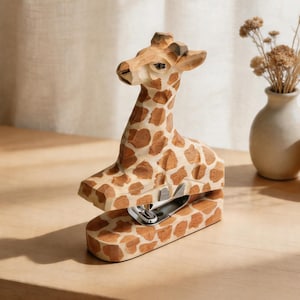May include: A giraffe-shaped wooden stapler, with a light brown body and dark brown spots. The giraffe's head and neck are intricately carved, with a metal stapling mechanism. The stapler is on a wooden surface.