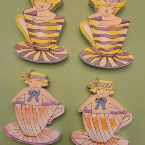 May include: Four wooden teacup figurines. Two teacups have yellow and purple stripes, and two have pink and orange stripes. Each figurine features a person wearing a hat and bow.