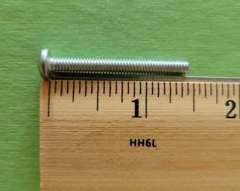 May include: A silver screw measuring 1 inch in length, placed on a wooden ruler.