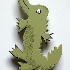 May include: A green wooden alligator figurine with a textured surface and a white eye. The alligator is standing on its hind legs with its mouth open.