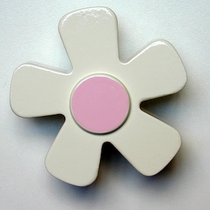 May include: A white flower-shaped ornament with a pink center. The ornament is made of wood and has a glossy finish.