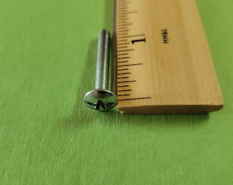 May include: A silver screw with a flat head and a Phillips drive. The screw is about 1 inch long and is next to a wooden ruler.