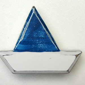 May include: A small wooden sailboat with a white hull and a blue sail. The sail is painted with a distressed look, giving it a vintage feel.