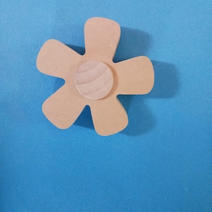 May include: A wooden flower-shaped craft element with five petals and a circular center. The flower is light brown, with a lighter wood grain pattern on the center. The background is a solid blue.