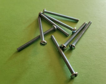 May include: A collection of silver-colored screws with slotted heads, scattered on a light green surface. The screws have a threaded shaft and a rounded head with a single slot for a screwdriver. The image is well-lit, highlighting the metallic sheen.