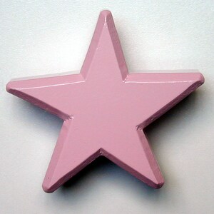May include: A solid, five-pointed star in a soft pink hue. The star has a slightly raised, beveled edge, giving it a three-dimensional appearance. The star is a decorative item, possibly for wall decor or craft projects.