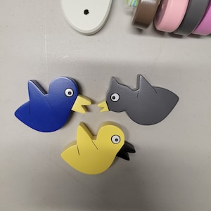 May include: Three wooden bird figurines, one blue, one gray, and one yellow. The birds are facing each other and have simple, cartoon-like features.