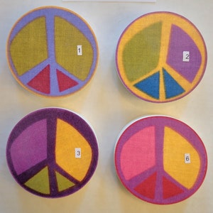 May include: Four round peace sign coasters with different color combinations. The coasters are made of a textured material and have a white background. The peace signs are in the following colors: 1) green, red, and blue, 2) green, purple, and blue, 3) purple, green, and yellow, and 4) pink, red, and yellow.