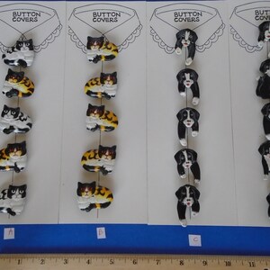 May include: A set of six button covers featuring black and white cats and black and white dogs. The button covers are arranged in four rows, with the cats in the first two rows and the dogs in the last two rows. The button covers are labeled A, B, C, and D.