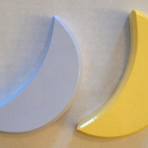 May include: Two crescent moon-shaped wall decor pieces. One is light blue and the other is yellow.