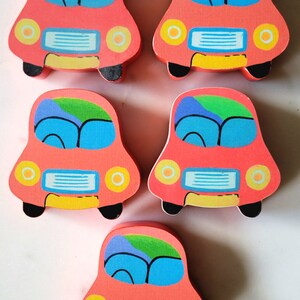 May include: Five wooden toy cars in a playful design. Each car is painted coral with blue, green, and yellow accents. The cars have black wheels and yellow headlights, perfect for children's play.