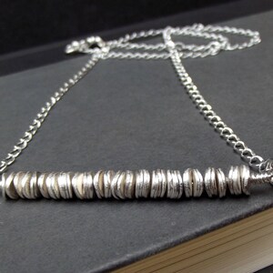 May include: A silver necklace with a long chain and a bar pendant made of stacked silver discs.