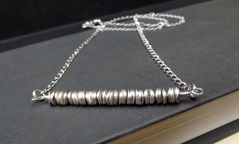 May include: A silver necklace with a long chain and a bar pendant made of stacked silver discs.