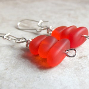 May include: A pair of silver earrings with red glass beads. The beads are stacked on top of each other and have a slightly irregular shape.