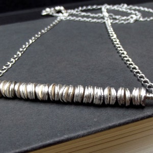 May include: A silver chain necklace with a pendant made of stacked silver discs.