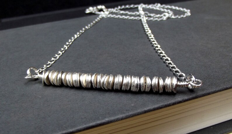 May include: A silver chain necklace with a pendant made of stacked silver discs.