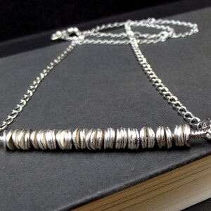 May include: A silver necklace with a chain and a bar pendant made of stacked silver discs.