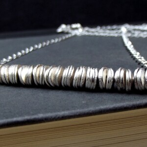 May include: A silver necklace with a long chain and a pendant made of stacked silver discs.