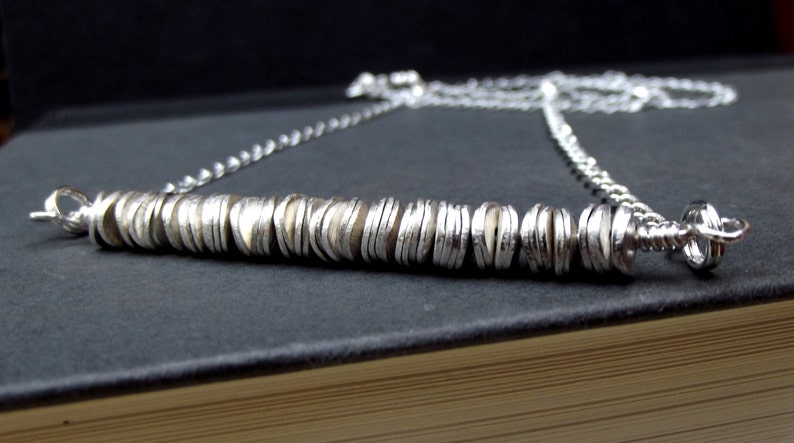 May include: A silver necklace with a long chain and a pendant made of stacked silver discs.