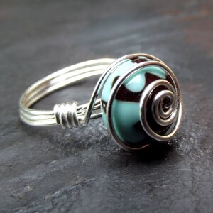May include: A silver ring with a turquoise and black patterned bead wrapped in silver wire.