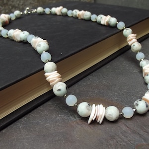 May include: A necklace made with light blue and white speckled beads, pink shell-shaped beads, and silver metal beads.