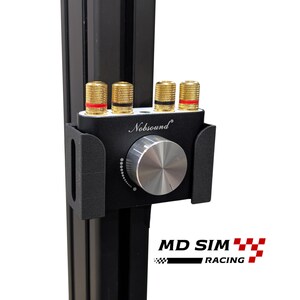 May include: A black Nobsound audio volume controller mounted on a vertical black aluminium extrusion profile. The device features a large silver circular knob, four gold-coloured speaker binding posts with red and black rings, and a black plastic mount.