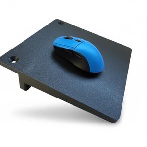 May include: A black, angled computer stand with a blue and black wireless mouse. The stand has a textured surface and is designed to elevate a laptop or keyboard. The mouse is positioned on the stand's surface.