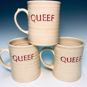 May include: Three white ceramic mugs with the word "QUEEF" written in red on each mug.