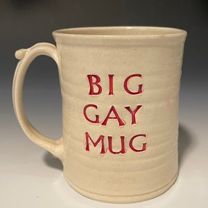 May include: A white ceramic mug with a red inscription that reads "BIG GAY MUG".