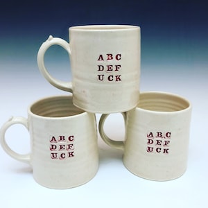 May include: Three white ceramic mugs with a red design that spells out "ABC DEF UCK" on each mug.