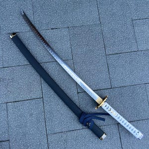 May include: A katana sword with a silver blade and a white handle with a diamond pattern. The sword has a black scabbard with a blue tie. The hilt is gold.