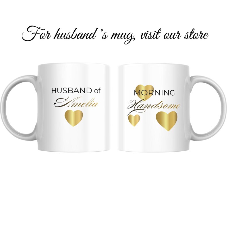 Op de afbeelding: Twee witte keramische mokken met zwarte en gouden tekst en gouden hartaccenten. Op de ene mok staat "HUSBAND of Amelia" en op de andere "MORNING Handsome". De mokken hebben een gebogen handvat.