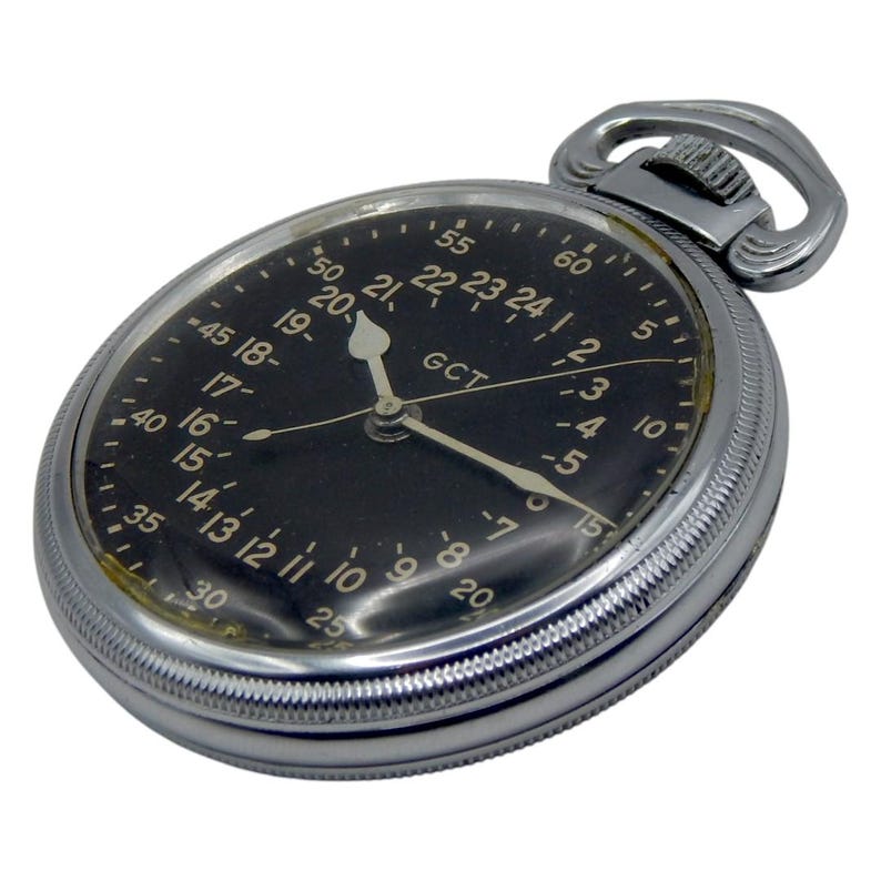 K&ouml;nnte beinhalten: Eine Vintage-Taschenuhr mit schwarzem Zifferblatt und silbernem Geh&auml;use. Die Uhr hat wei&szlig;e Ziffern und Zeiger, mit dem Text "GCT" sichtbar. Die Uhr hat oben eine Schlaufe f&uuml;r eine Kette.