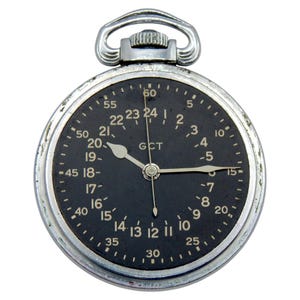 K&ouml;nnte beinhalten: Eine Vintage-Taschenuhr mit schwarzem Zifferblatt und silbernem Geh&auml;use. Die Uhr hat wei&szlig;e Ziffern und Zeiger, mit dem Text "GCT" in der Mitte. Sie hat oben eine Schlaufe zum Anbringen einer Kette.