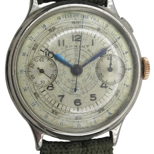 Pode incluir: Relógio de pulso vintage prateado com mostrador creme. Apresenta vários submostradores, ponteiros azuis e a palavra "SPRINT". A bracelete é de tecido verde e a coroa dourada. O diâmetro do mostrador é de aproximadamente 3,5 cm.