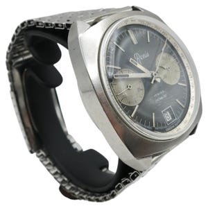 May include: A vintage silver-toned wristwatch with a dark gray face and two sub-dials. The watch features the name "Penis" on the face, along with the text "17 Rubis Incabloc" and a date window. The watch has a metal band and a black strap.