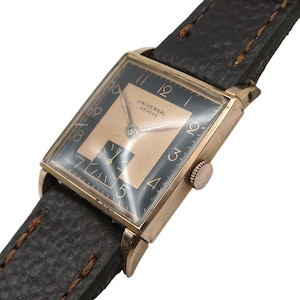 Puede incluir: Un reloj de pulsera vintage dorado con esfera negra y correa de cuero. La esfera del reloj tiene números y agujas doradas, con el texto "UNIVERSAL GENEVE". El reloj rectangular tiene una pequeña corona en el lateral.