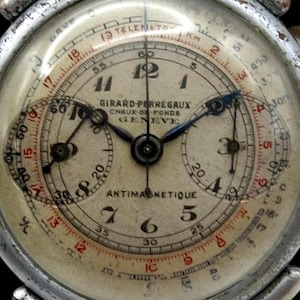 Pode incluir: Relógio cronógrafo Girard-Perregaux vintage com mostrador creme, ponteiros e algarismos pretos. O relógio tem dois submostradores e uma caixa de metal prateado. O texto "ANTIMAGNETIQUE" é visível.